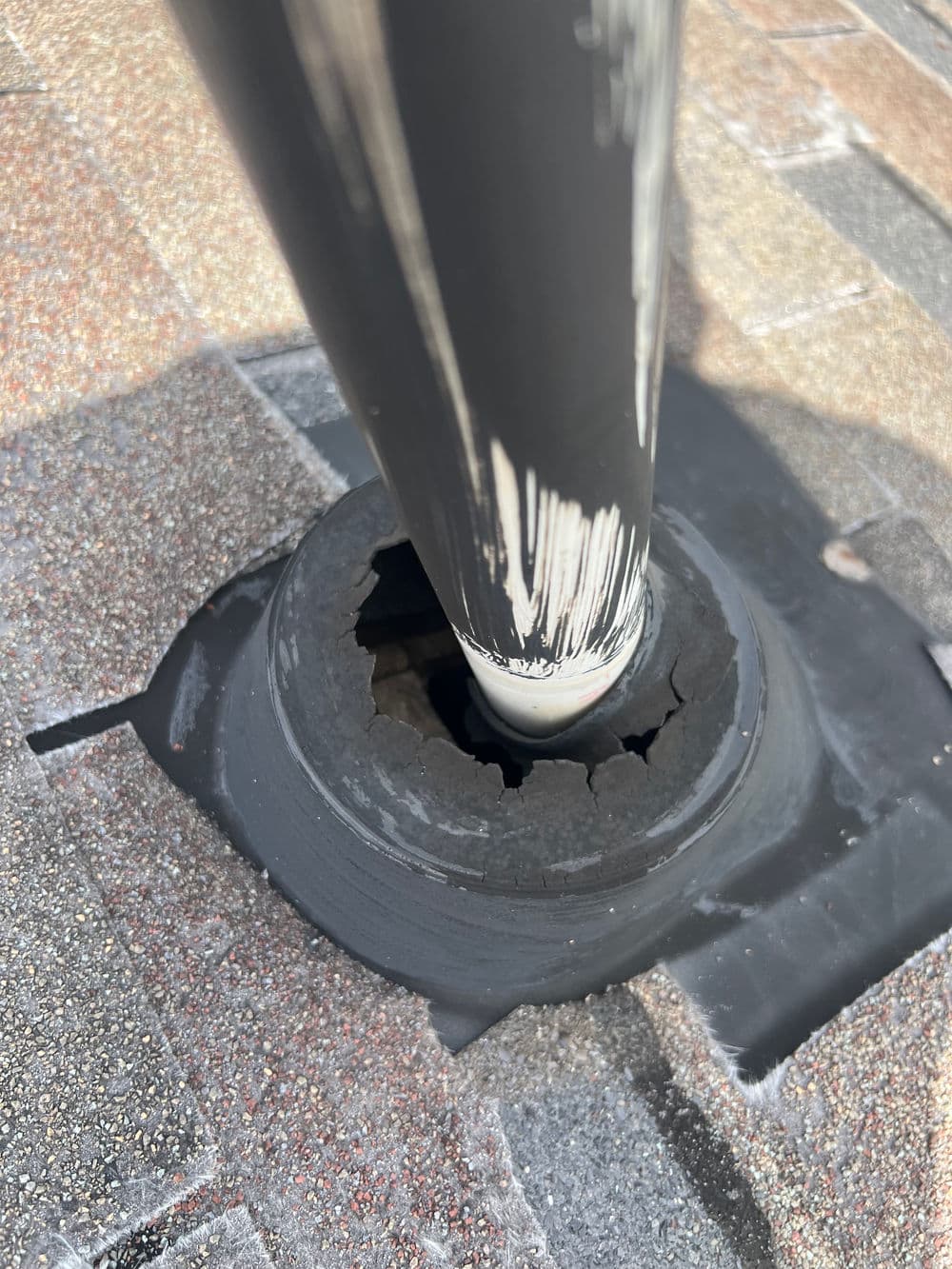 Damaged roof flashing around a pipe, showing cracks and wear on asphalt shingles.