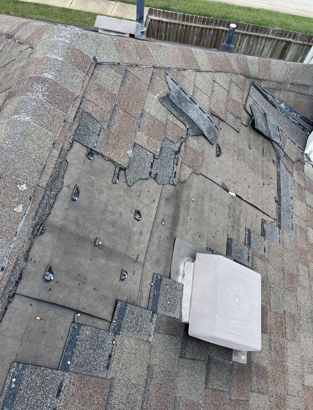 Damaged roof shingles and exposed underlayment with ventilation installation visible.